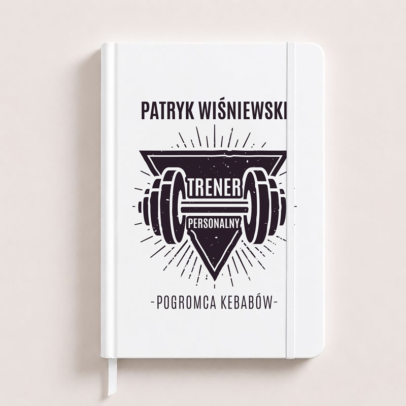Notatnik z białą okładką, na której znajduje się napis "PATRYK WIŚNIEWSKI TRENER PERSONALNY" oraz grafika ciężarów. Pod napisem widnieje hasło "-POGROMCA KEBABÓW".