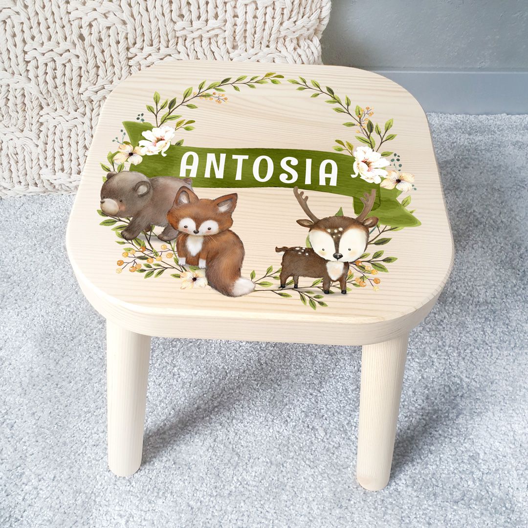 Drewniany stołek dla dziecka z grafiką na siedzisku, która przedstawia leśne zwierzątka, roślinki oraz imię na zielonym tle szarfy