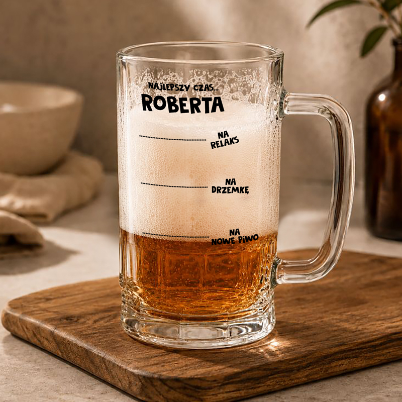 Szkło do piwa z napisem "Najlepszy czas Roberta" oraz poziomami do relaksu, drzemki i nowego piwa, stojące na drewnianym podkładce.