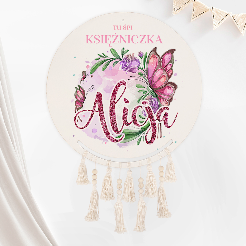 Okrągła ozdoba ścienna z napisem 'Aliga' w artystycznym stylu, otoczona dekoracyjnymi motylami i kwiatami, z frędzlami na dole w neutralnych odcieniach.