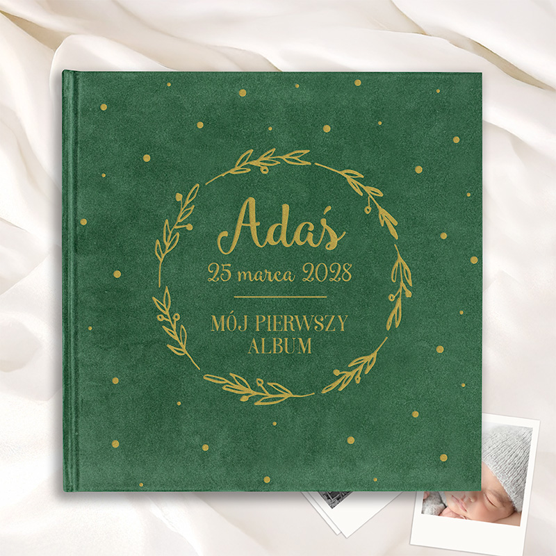 Zielona okładka albumu z ozdobnym napisem "Adaś 25 marca 2028 Mój pierwszy album" otoczonym złotymi liśćmi.