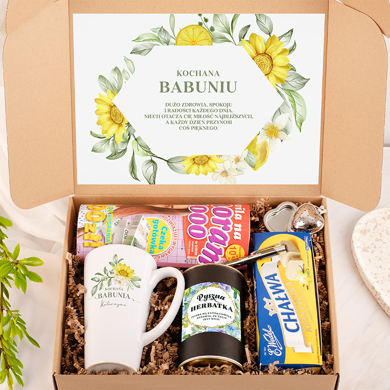 Kartonik z podarunkiem dla babci, zawierający kubek z napisem "Kochana Babunia", herbatkę w czarnej puszce, chałwę i słodycze, z ozdobnym listem na wieczku z rysunkiem kwiatów i życzeniami zdrowia i spokoju.