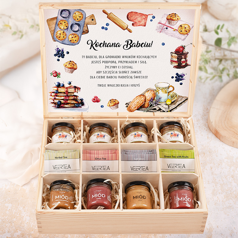 Elegancka drewniana skrzynka z napisem "Kochana Babciu!" na wewnętrznej stronie wieka, zawierająca dziesięć słoiczków z miodem i herbatami, poukładanych w naturalnym wypełnieniu. W środku znajdują się różne smaki herbaty, takie jak ziołowa, cytrusowa oraz zielona z owocami, a także słoiczki z miodem w różnych kolorach. Całość prezentowana na delikatnym tle.