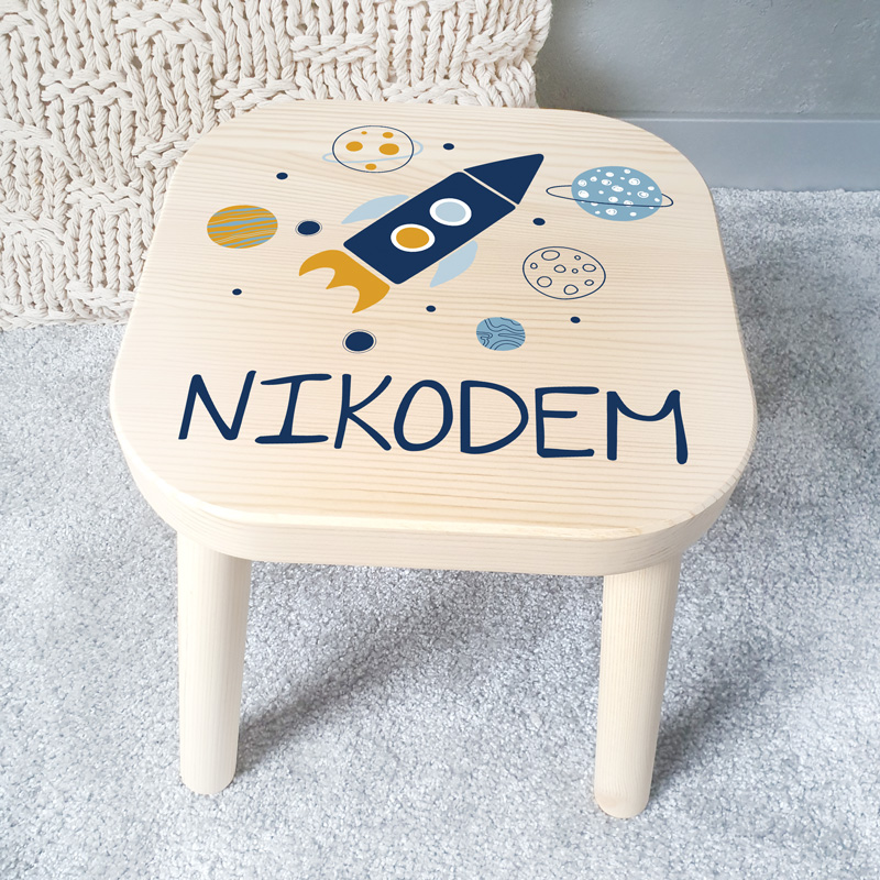 Stołek drewniany dziecięcy w jasnym kolorze z personalizowanym nadrukiem na siedzisku z motywem kosmicznej przygody i imieniem dziecka.