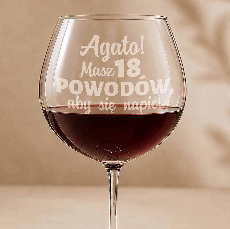 W dużym kieliszku wina znajduje się czerwona ciecz, a na szkle wygrawerowany jest tekst: "Agato! Masz 18 powodów, aby się napić!"