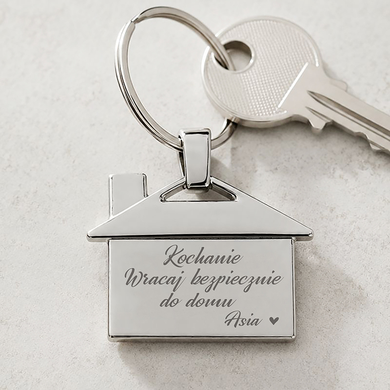 Srebrny breloczek w kształcie domu z wygrawerowanym napisem „Kochanie, Wracaj bezpiecznie do domu, Asia ♥”.