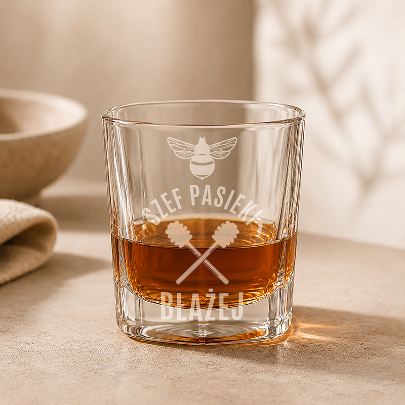Szklanka z whisky, z wygrawerowanym napisem "Szef Pasieki Błażej" oraz wzorem w kształcie pszczół i łyżek do miodu.