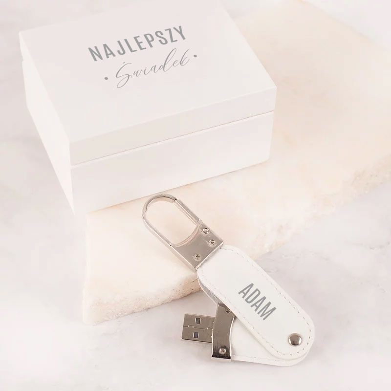 Biały pendrive w skórzanej osłonie, obok elegancka biała pudełko z napisem "NAJLEPSZY ŚWIADEK".