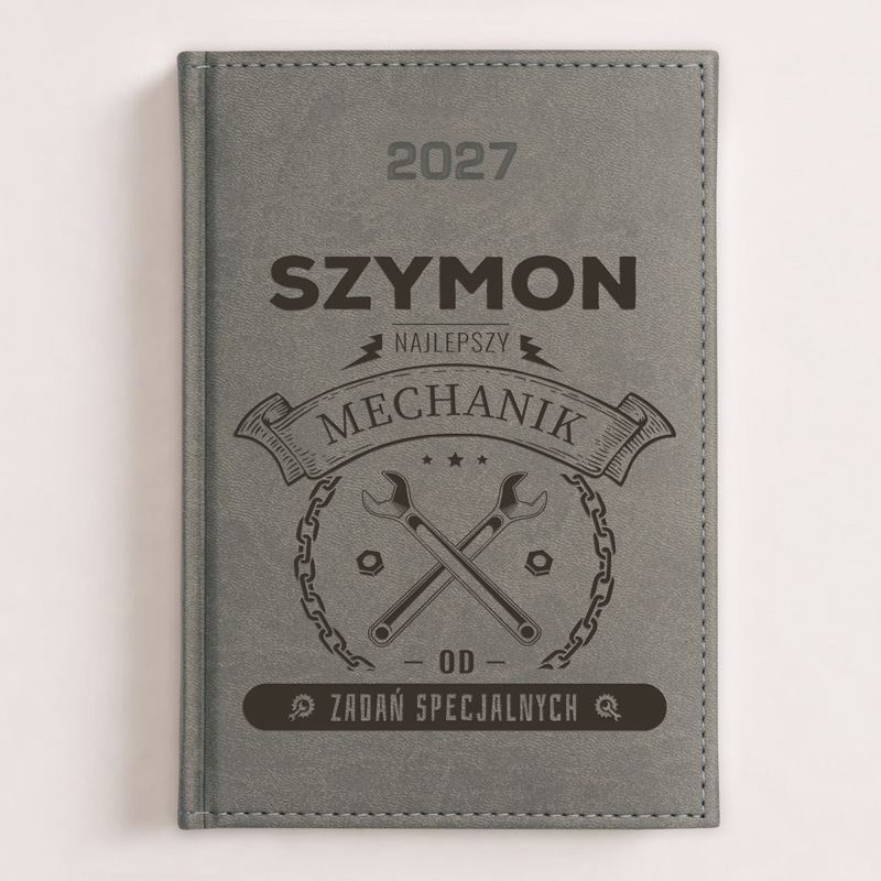 Szary notes z napisem "SZYMON NAJLEPSZY MECHANIK 2027" oraz grafiką dwóch kluczy mechanicznych.