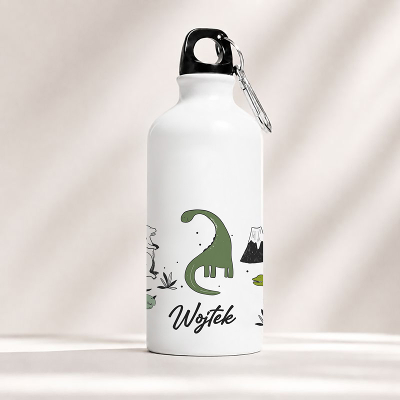 Biała butelka ze zielonym dinozaurem i napisem "Wojtek", ozdobiona ilustracjami przyrody.