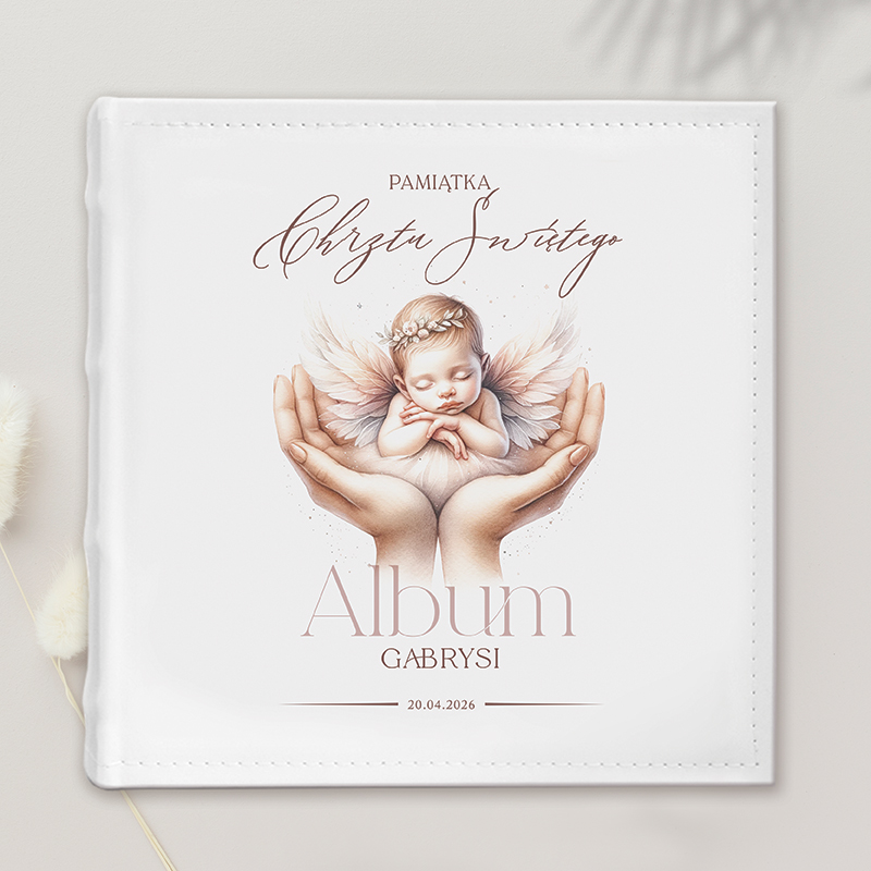 Okładka albumu pamiątkowego z wizerunkiem śpiącego niemowlęcia z anielskimi skrzydłami, trzymanego w dłoniach. Na okładce widnieje napis 'Pamiątka Chrztu Świętego' oraz imię 'Gabrysi' i data '20.04.2026'.