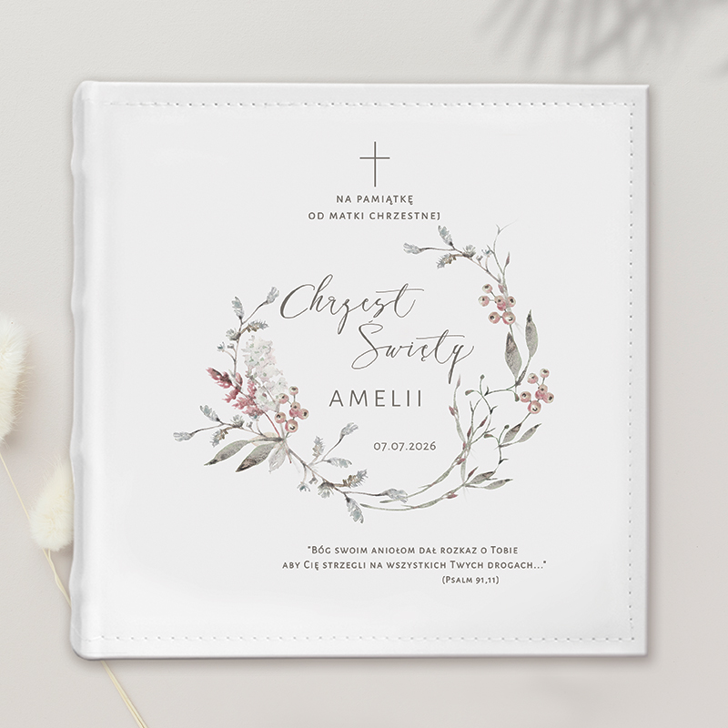 Biała okładka z dekoracyjnym wzorem kwiatowym, na której widnieje napis 'Chrzest Święty Amelii', data 07.07.2026 oraz cytat biblijny z Psalmów 91,11. W górnej części umieszczony jest krzyż.