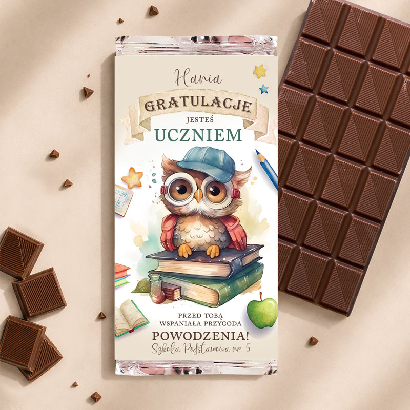 Czekolada z opakowaniem przedstawiającym uśmiechniętą sowę w czapce, z książkami w tle i napisem "Gratulacje jesteś uczniem".