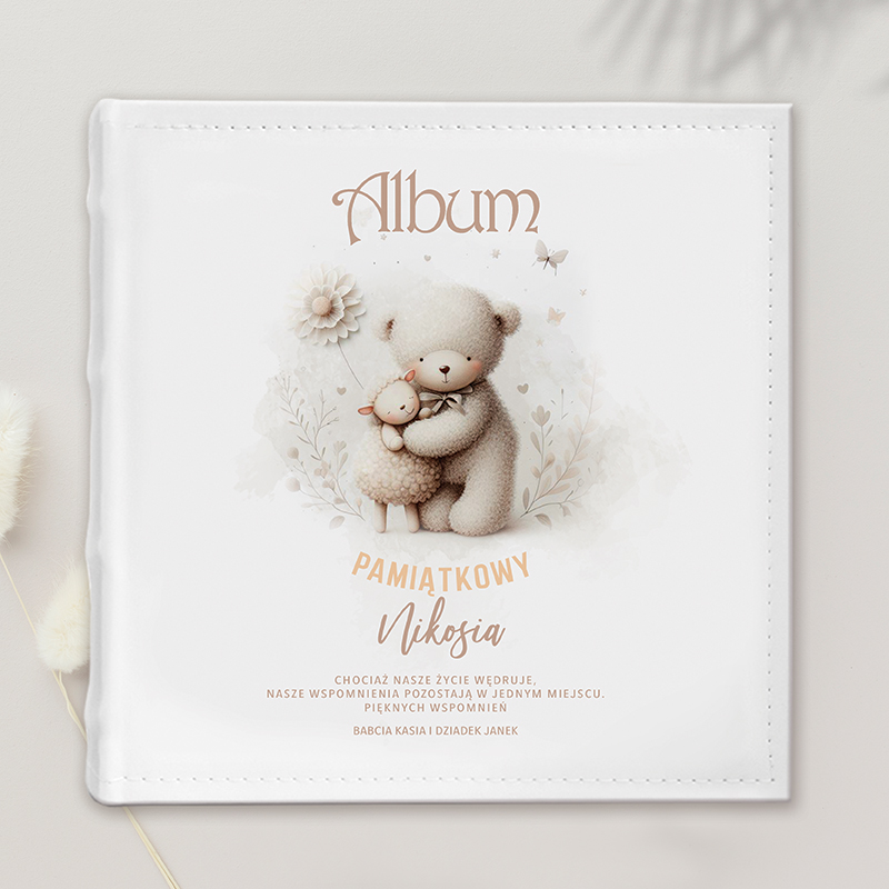Biały album na zdjęcia z ilustracją misia trzymającego owieczkę, z napisem 'Album Pamiątkowy Nikosia' oraz cytatem o wspomnieniach, otoczony delikatnymi kwiatami.