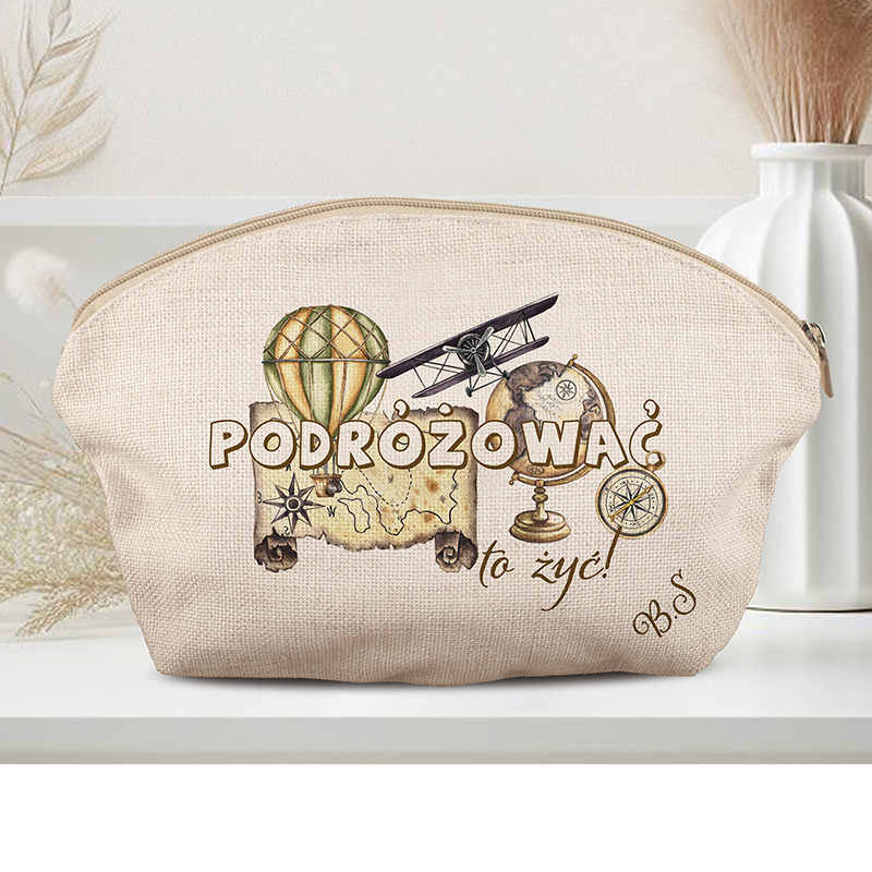 Kosmetyczka z ilustracjami związanymi z podróżami, w tym balonem na gorące powietrze, samolotem, mapą i globusem, z napisem 'PODRÓŻOWAĆ to żyć!' na beżowym tle.
