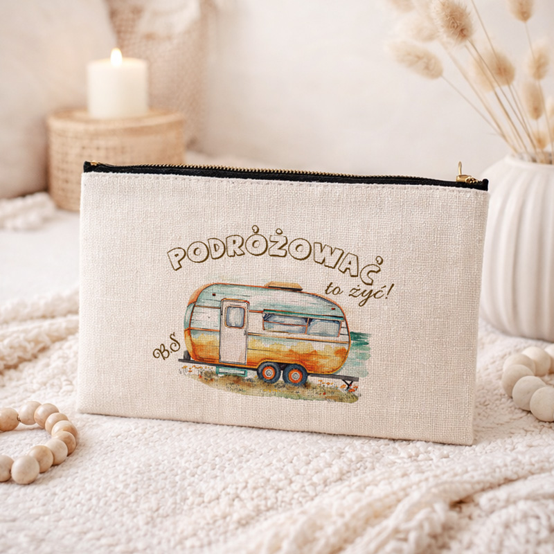 Kosmetyczka w jasnym kolorze z rysunkiem przyczepy kempingowej i napisem "PODRÓŻOWAĆ to żyć!" na przedniej stronie.