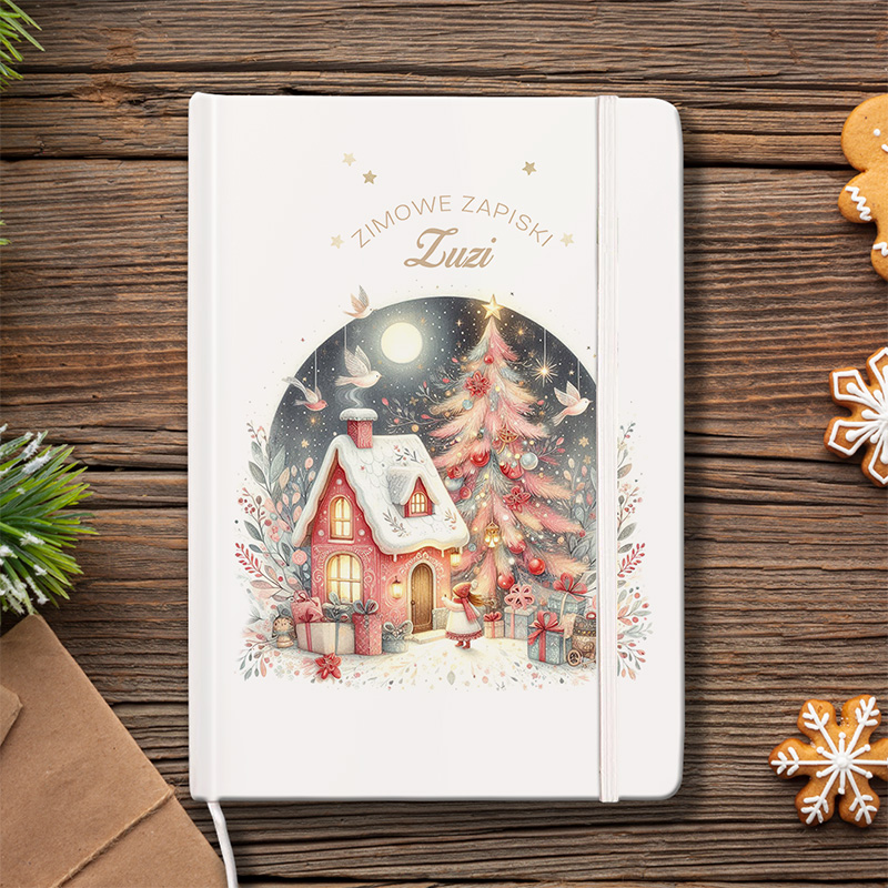 Notes z zimowym motywem, przedstawiający różowy domek z śniegiem na dachu, choinkę ozdobioną bombkami, prezenty oraz postać dziecka, w otoczeniu ptaków i śnieżnych gałęzi, na drewnianym tle.