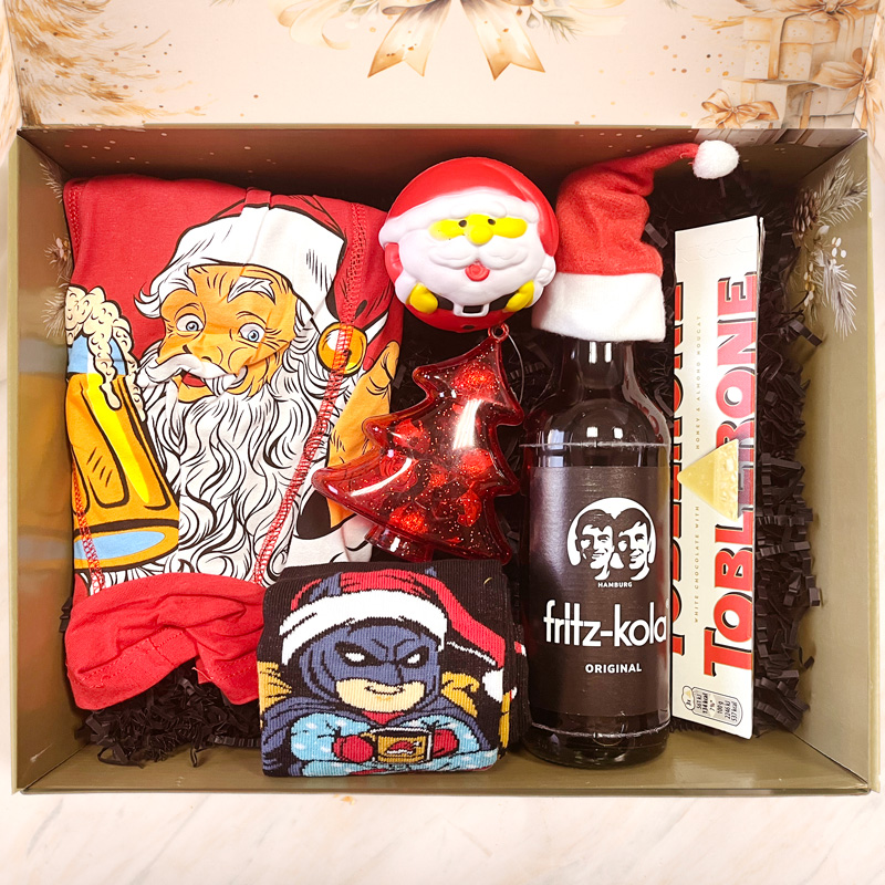 Zestaw prezentowy z kolorowymi skarpetkami oraz motywem Świętego Mikołaja, czerwoną choinką jako dekoracją, napojem fritz-kola, małym Mikołajem i czekoladą Toblerone w eleganckim opakowaniu.