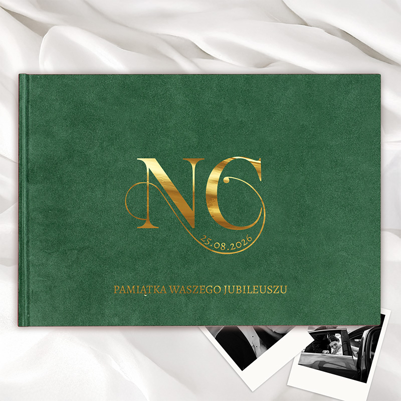 Zielona okładka albumu z złotym napisem "NC" oraz datą "25.08.2026" i napisem poniżej "PAMIĄTKA WASZEGO JUBILEUSZU", leżąca na białej tkaninie z kilkoma czarno-białymi zdjęciami obok.