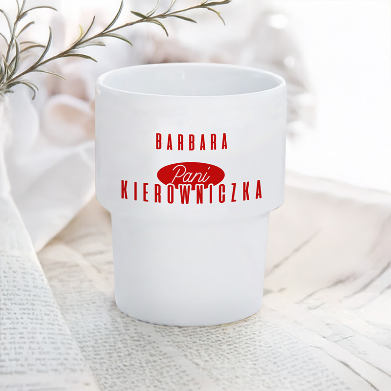 Biały kubek z napisem "Barbara Pani Kierowniczka" w czerwonym kolorze, leżący na białym tle.