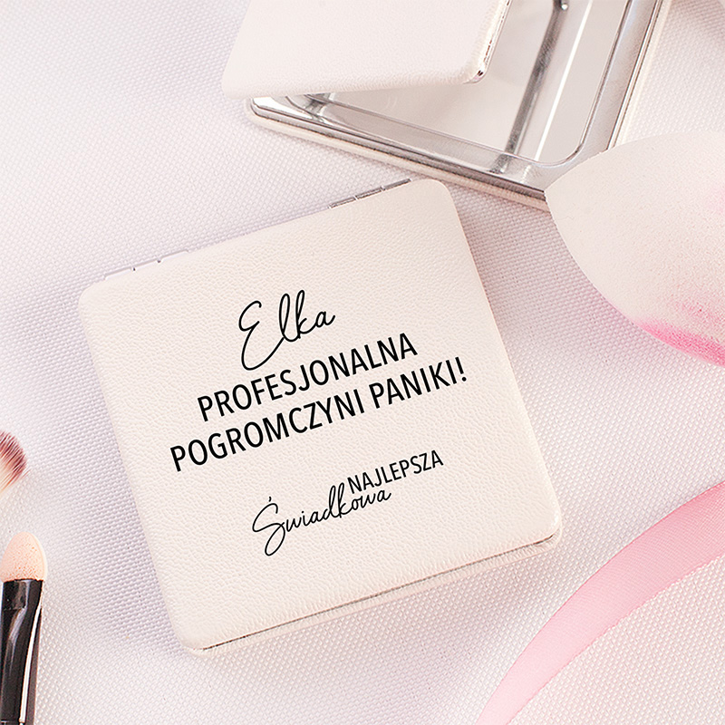 Biały lusterko z napisem "Ella PROFESJONALNA POGROMCZYNI PANIKI! ŚWIADKOWA NAJLEPSZA" na tle różowych akcesoriów kosmetycznych.