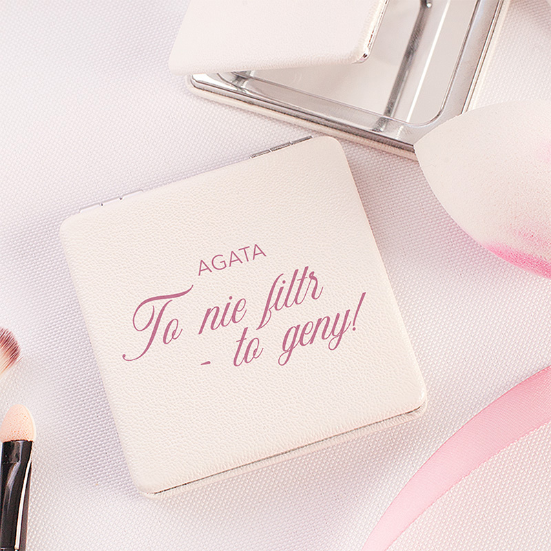 Kompaktowy puder w białej, skórzanej oprawie z napisem 'To nie filtr - to geny!' oraz logo AGATA, otoczony akcesoriami do makijażu, takimi jak gąbeczka oraz pędzle na jasnym tle.