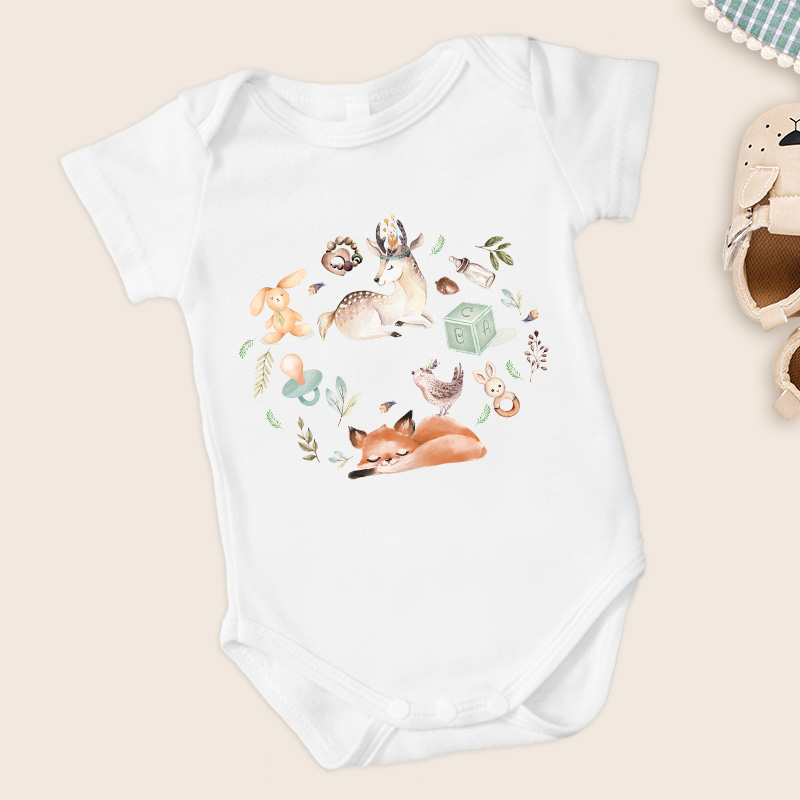 Biały body dziecięce z ilustracją zwierząt, w tym lisa, sarny, królika oraz elementów zabawkowych i roślinnych, na jasnym tle.