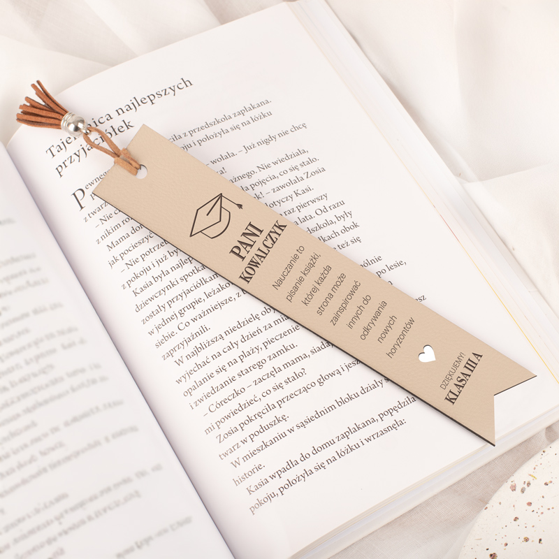 Znak do książki z tekstem "Pani Kowalczyk" oraz informacjami o nauczycielu, w zielonym kolorze i stylizowanym rysunku czapki absolwenta, umieszczony na stronie otwartej książki.