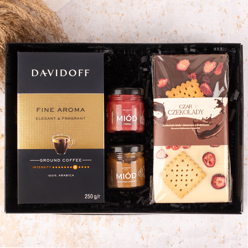 Zestaw upominkowy zawierający kawę mieloną Davidoff Fine Aroma, dwa słoiczki miodu w różnych smakach oraz tabliczkę czekolady o smaku białej czekolady z dodatkami, znajdujący się w czarnym opakowaniu.
