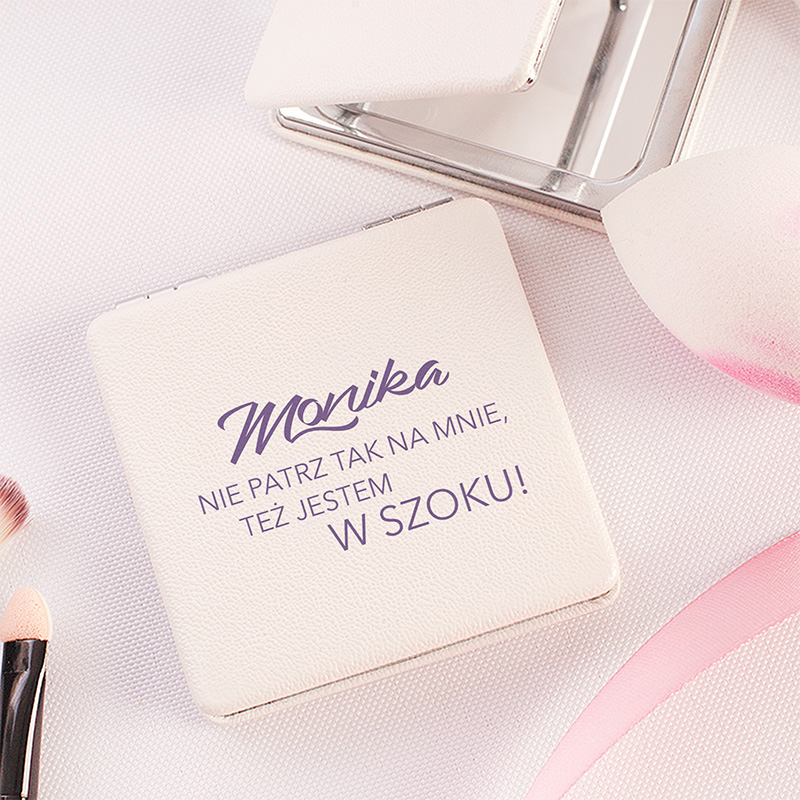 Lusterko w kolorze białym z napisem 'Monika' i hasłem 'NIE PATRZ TAK NA MNIE, TEŻ JESTEM W SZOKU!', otwarta z lusterkiem obok oraz narzędziami do makeupu.