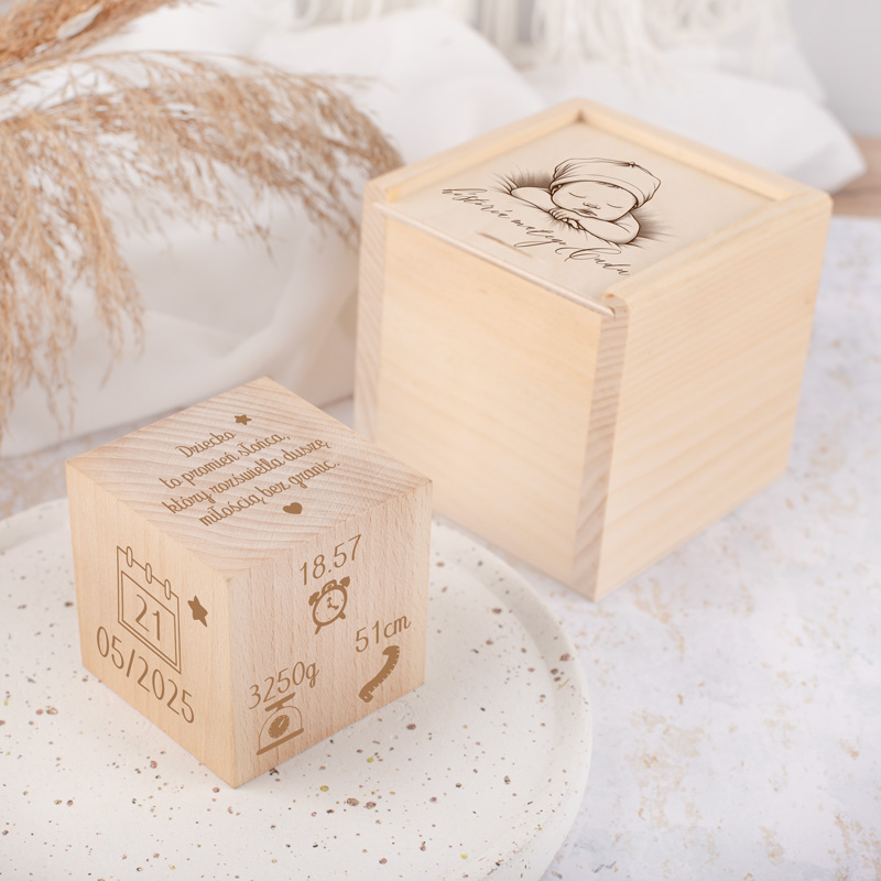 Dwa drewniane pudełka, jedno z wygrawerowanymi danymi narodzin (data, czas, waga, wzrost), a drugie z wizerunkiem niemowlęcia. Pudełka na stonowanym tle z ozdobnymi roślinami w tle.