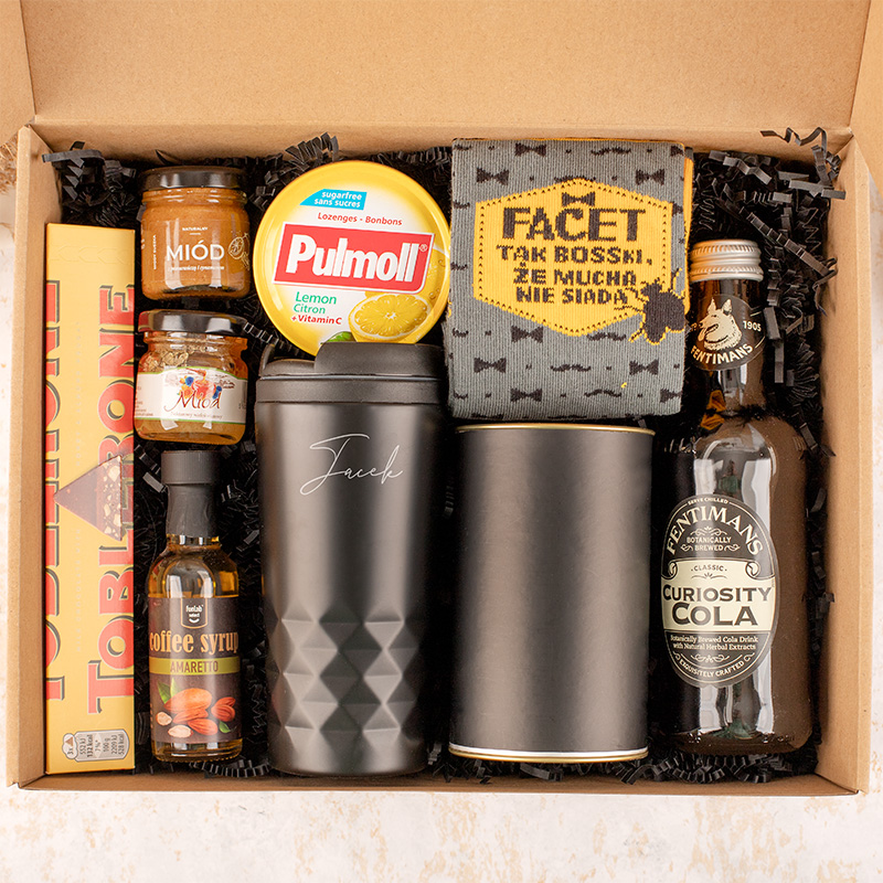 Zestaw upominkowy w kartonowym pudełku, zawierający herbatę Pulmoll, syrop kawowy, miód, skarpetki z napisem, kubek termiczny oraz butelki z napojami, w tym Curiosity Cola.