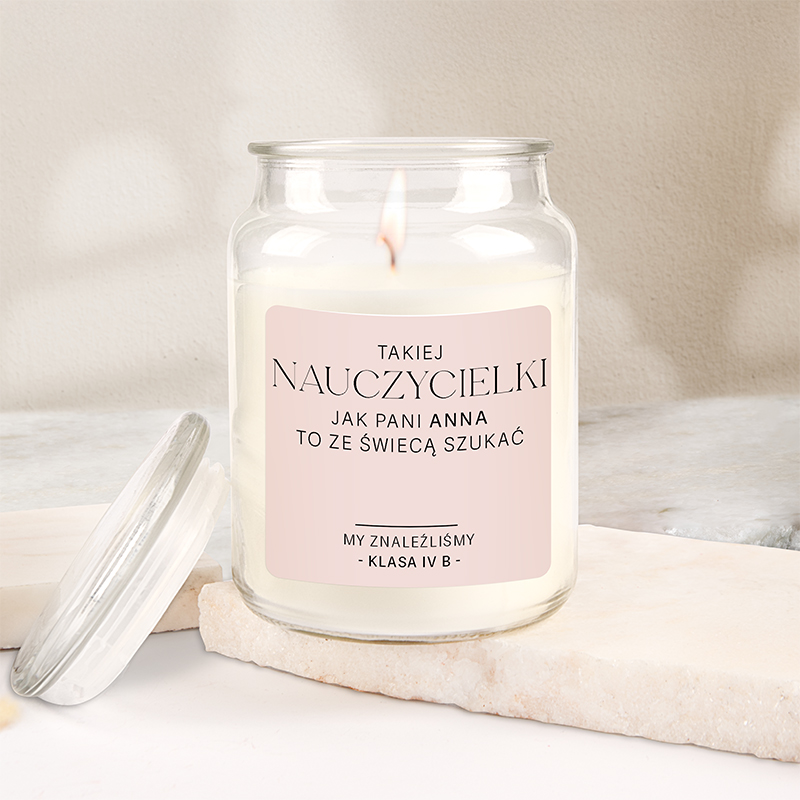 Szklany słoik ze świecą, na etykiecie znajduje się napis: 'Takiej nauczycielki jak pani Anna to ze świecą szukać. My znaleźliśmy – klasa IV B'. Słoik jest ustawiony na jasnym tle z marmuru.