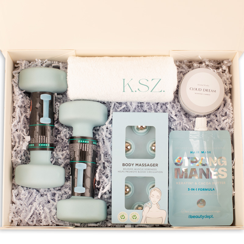 Zestaw do pielęgnacji zawierający dwa lekkie hantle w kolorze miętowym, masażer do ciała, świecę zapachową 'Cloud Dream', ręcznik z napisami oraz maskę do włosów w saszetce, wszystko umieszczone w eleganckim pudełku z papierowym wypełnieniem.
