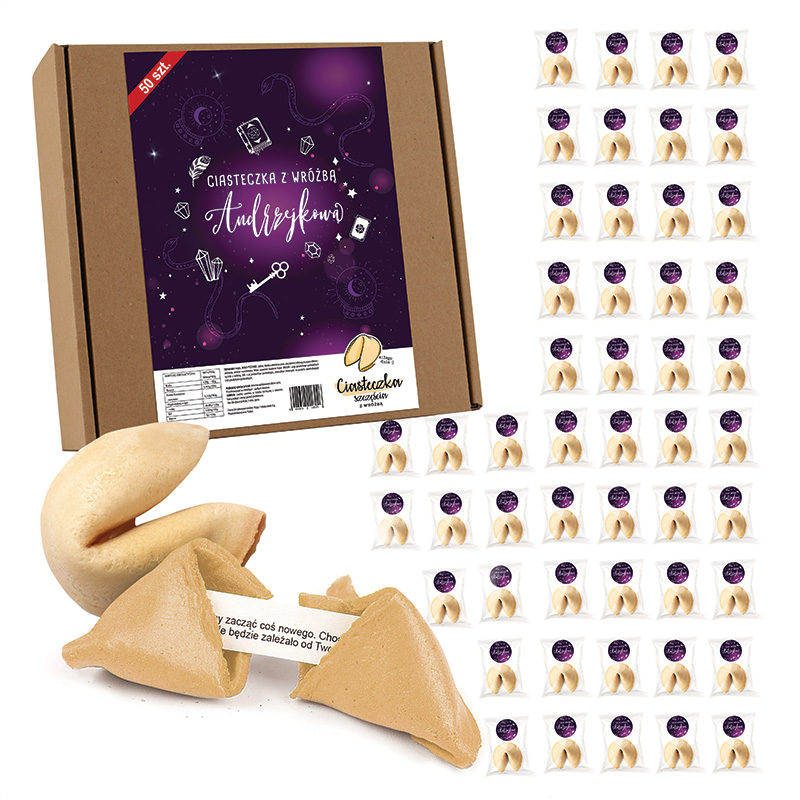 Opakowanie z ciastkami wróżby na ciemnym tle z grafiką i napisem "Ciastka z wróżbą Andrzejkową". Wewnątrz widoczne ciastka w kształcie wróżb, z jednym ciastkiem rozłamanym, pokazującym wróżbę w środku. Obok opakowania znajduje się wiele pojedynczo zapakowanych ciastek.