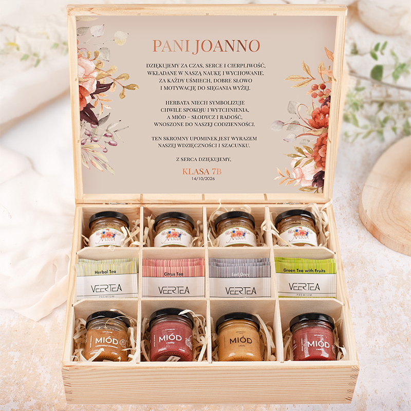 Drewniane pudełko z herbatami i miodem, z dedykacją dla Pani Joanny, z różnymi rodzajami herbat, w tym ziołową, cytrusową i zieloną z owocami, umieszczonymi w słoiczkach, oraz słoikami miodu, ozdobione kwiatowym motywem na pokrywce, z napisem 'Klasa 7B' i datą 14/10/2026.