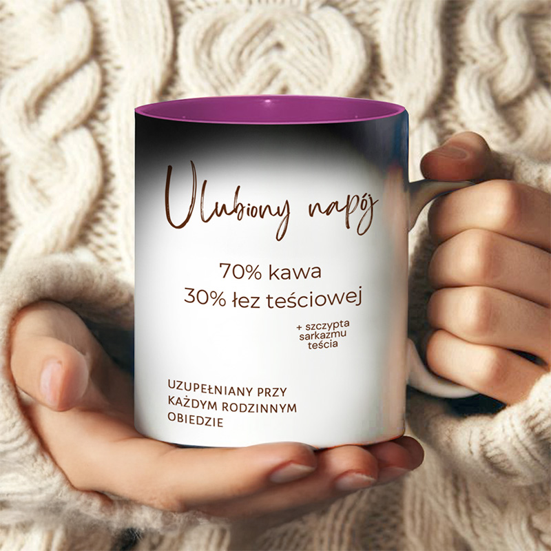 Kubek z napisem 'Ulubiony napój' zawierający tekst: '70% kawa, 30% też teściowej' oraz '+ szczypta sarkazmu teścia', trzymany w rękach osoby w swetrze z grubym splotem.
