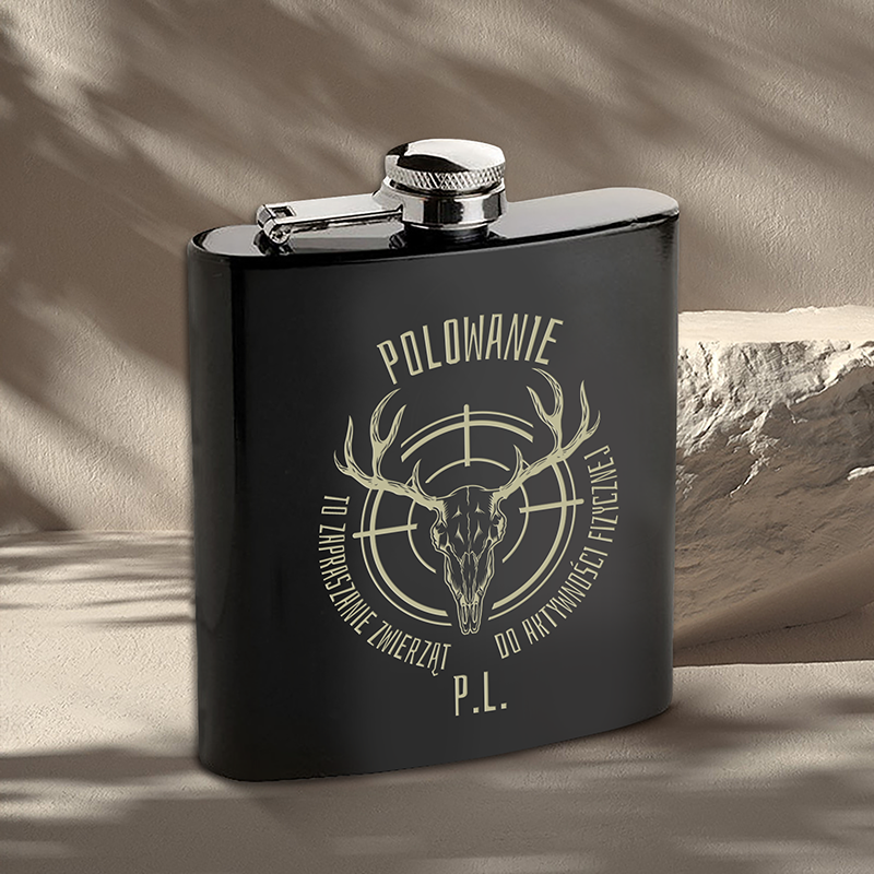 Czarna piersiówka z metalową zakrętką, na której znajduje się złoty nadruk z czaszką jelenia, rogami i napisem "POLOWANIE TO ZAPRASZANIE ZWIERZAT DO AKTYWNOŚCI FIZYCZNEJ P.L."