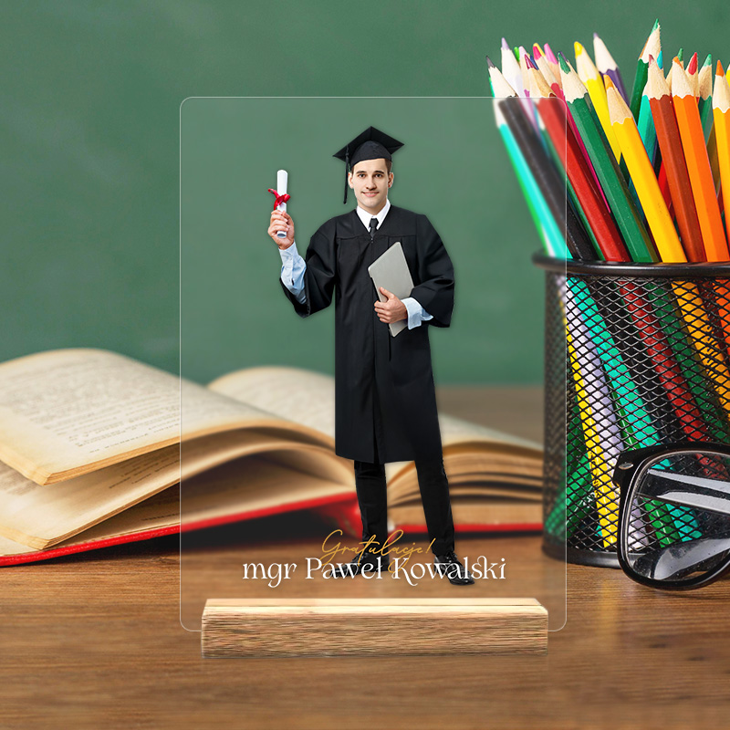 Mężczyzna w todze i birecie trzyma dyplom w jednej ręce i tablet w drugiej, stojąc na tle zielonej tablicy. W tle widoczne są otwarte książki oraz pojemnik z kolorowymi ołówkami i okulary.