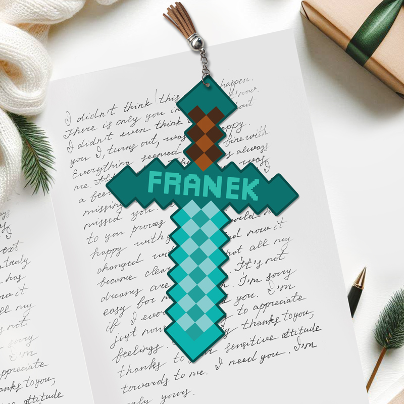 Zawieszka w kształcie miecza z gry Minecraft, w kolorze niebieskim i brązowym, z imieniem 'FRANEK' na hilt, umieszczona na tle ręcznie napisanej kartki z pozdrowieniami i prezentu zapakowanego w brązowy papier z zieloną wstążką.