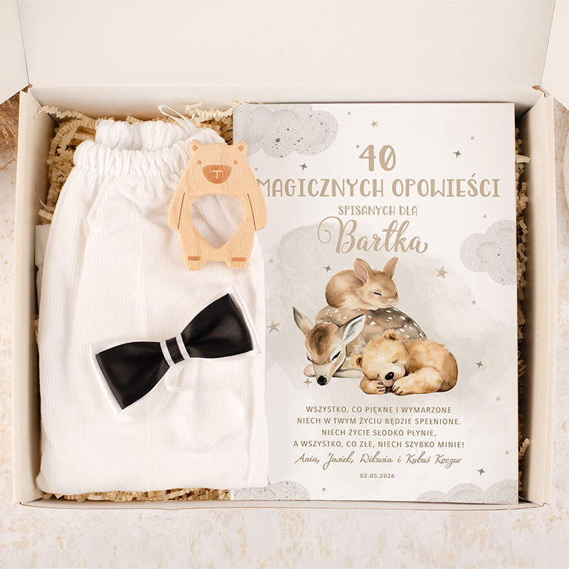 Zestaw prezentowy zawierający białe spodenki, czarną muszkę, drewniany gryzak w kształcie misia oraz książkę "40 magicznych opowieści spisanych dla Bartka" z ilustracjami zwierząt, wszystko umieszczone w ozdobnym pudełku.