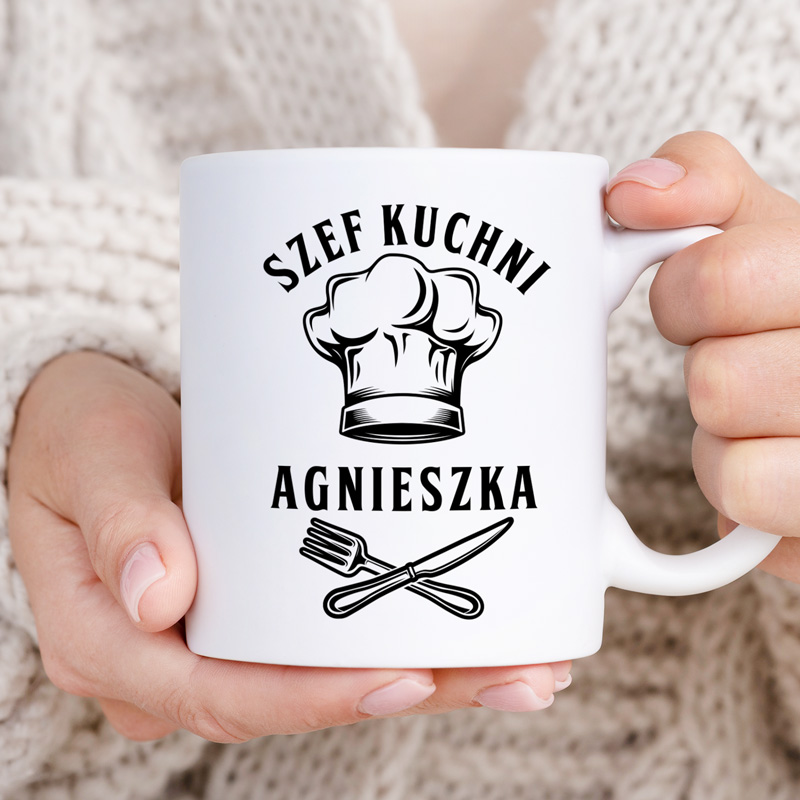 Osoba trzyma białą filiżankę z nadrukiem przedstawiającym szefa kuchni, widoczne napisy "SZEF KUCHNI AGNIESZKA" oraz ikony widelca i noża.