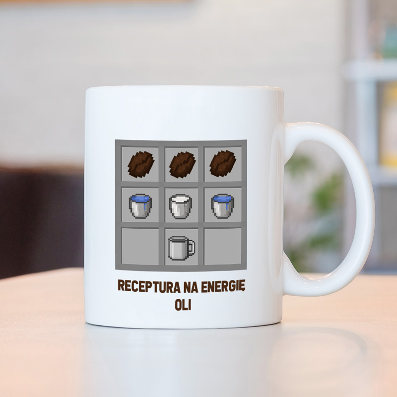 Biała filiżanka z grafiką przedstawiającą wzór przepisu, składający się z surowców do stworzenia energii, z napisem 'RECEPTURA NA ENERGIE OLI' u dołu. Tło w lekko rozmytym wnętrzu.