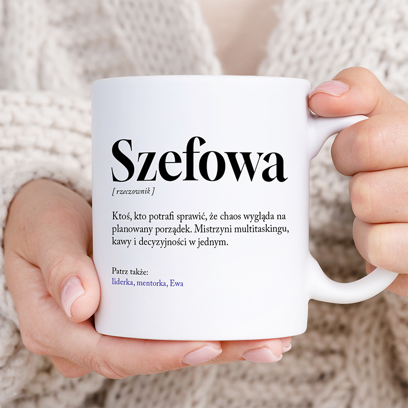Kubek trzymany przez osobę, z napisem "Szefowa" oraz definicją w języku polskim, przedstawiającą osobę potrafiącą zorganizować chaos. Tło jest jasne, a ręka delikatna, w dodatku widoczna jest partia jasnego swetra.