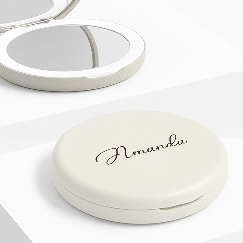 Eleganckie lusterko w etui w kolorze jasnym z imieniem 'Amanda' napisanym brunatnym stylem kaligraficznym na górnej części, obok leży otwarte lusterko.