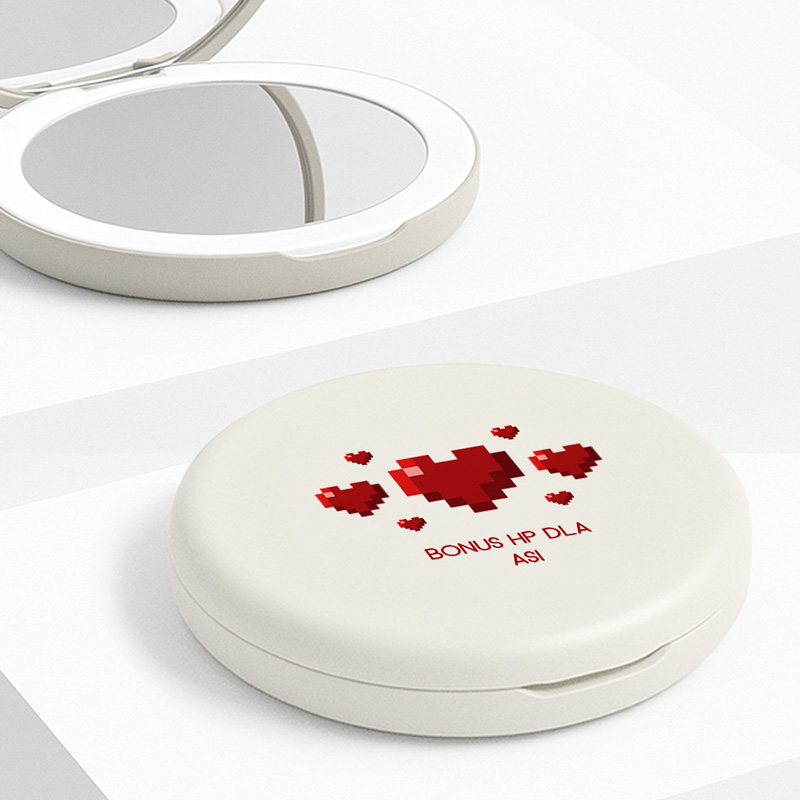 Okrągłe lusterko w oprawie w kolorze jasnym z nadrukiem w stylu pixel art przedstawiającym czerwone serca oraz napisem 'BONUS HP DLA ASI'. W tle znajduje się zamknięte drugie lusterko.