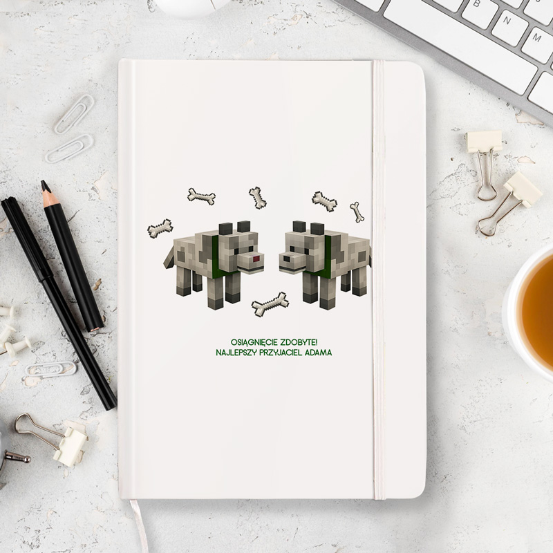 Wizualizacja okładki notesu z grafiką dwóch psów z gry Minecraft, otoczonych kościami, z napisem "Osiągnęcie zdobyte! Najlepszy przyjaciel Adama".