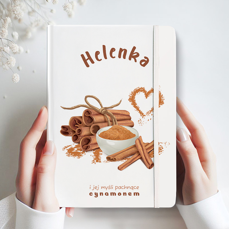 Zamknięty notes z białą okładką, na którym znajduje się napis 'Helenka' oraz ilustracja z cynamonem w formie zawiniętych bruszków, miseczki z cynamonem w proszku i kilku dodatkowych lasek cynamonu, z towarzyszącym tekstem 'i jej myśli pachnące cynamonem'.