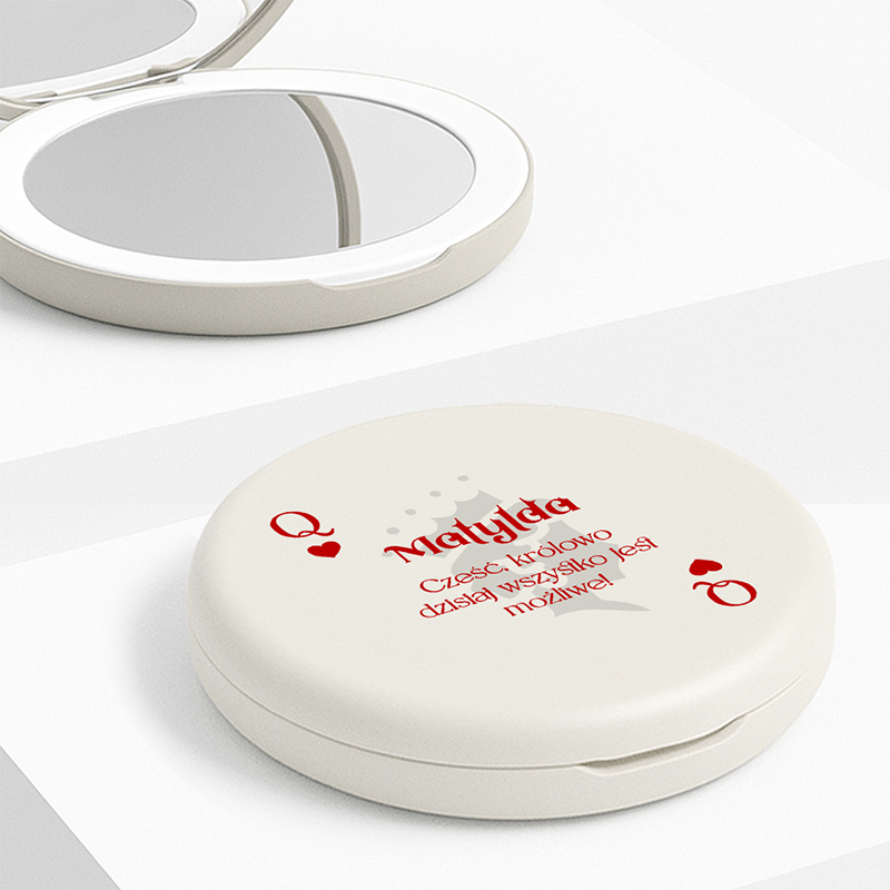 Zamknięte lusterko w kolorze kremowym z napisem 'Małgorzata' oraz hasłem 'Cześć, królowo dzisiaj wszystko jest możliwe' w czerwonych literach, leżące na tle jasnej powierzchni.