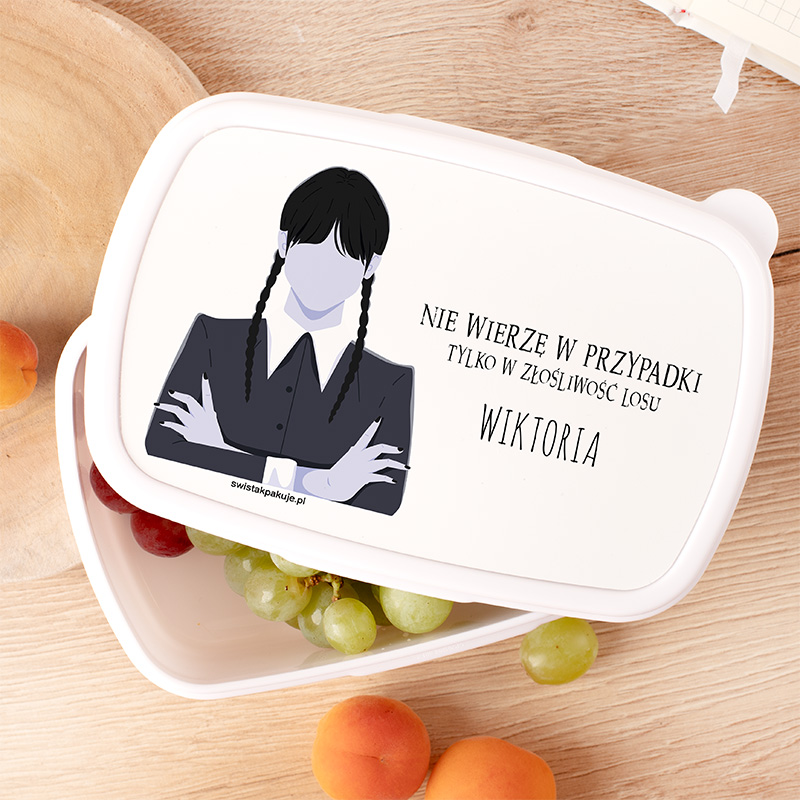 Pojemnik na jedzenie z ilustracją postaci o ciemnych, splecionych warkoczach, ubranej w czarną bluzkę i białą koszulę, z podpisem "NIE WIERZĘ W PRZYPADKI TYLKO W ZŁOŚLIWOŚĆ LOSU WIKTORIA". Na tle pojemnika widoczne owoce: winogrona i brzoskwinie.